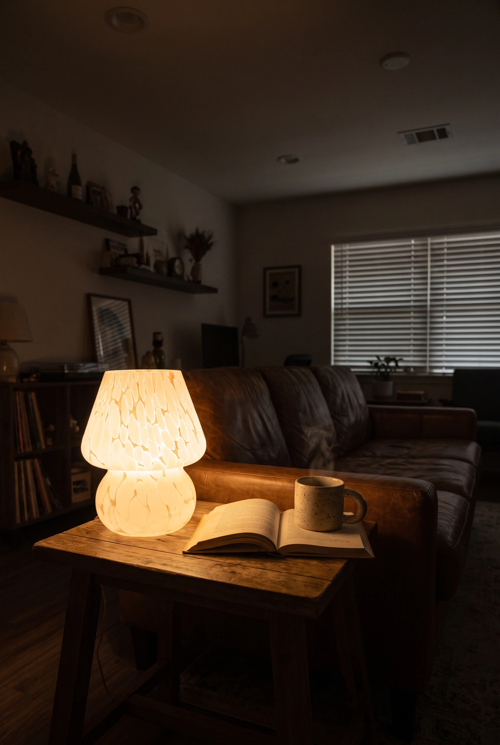 Small glass mushroom lamp glowing warmly on a side table in a dim apartment living room